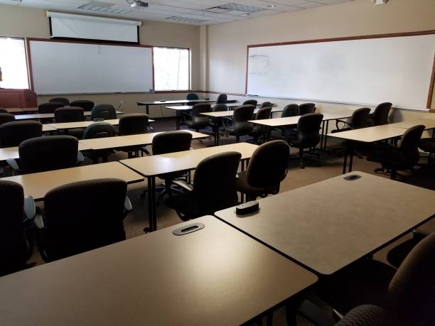 Classroom view from left rear towards front with tables, chairs, whiteboard, and projection screen