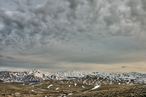Distant snow peaked mountain tops across the dry and brown valley under the cloudy sky