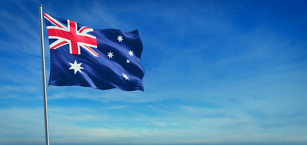 The National flag of Australia blowing in the wind in front of a clear blue sky