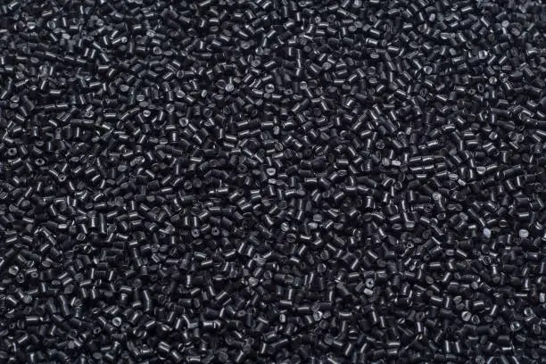 CLOSE-UP FLAT LAY OF BLACK POLYMER GRANULES ON GLASS TABLE