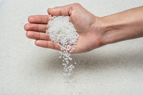 CLOSE-UP OF PLASTIC POLYMER GRANULES SPREAD ON EVEN SURFACE CLOSE-UP FLAT LAY OF WHITE POLYMER GRANULES ON GLASS TABLE WITH HUMAN HAND HOLDING, CHECKING THE GRANULES AND DROPPING BACK ON TABLE polypropylene stock pictures, royalty-free photos & images