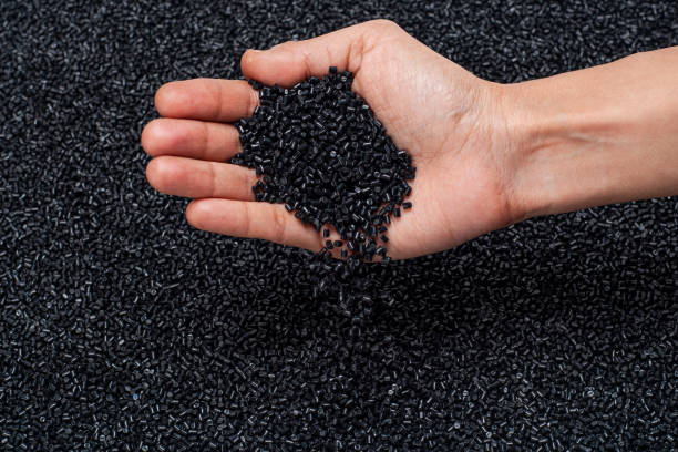 CLOSE-UP OF PLASTIC POLYMER GRANULES SPREAD ON EVEN SURFACE CLOSE-UP FLAT LAY OF BLACK POLYMER GRANULES ON GLASS TABLE WITH HUMAN HAND HOLDING, CHECKING THE GRANULES AND DROPPING BACK ON TABLE rubber stock pictures, royalty-free photos & images