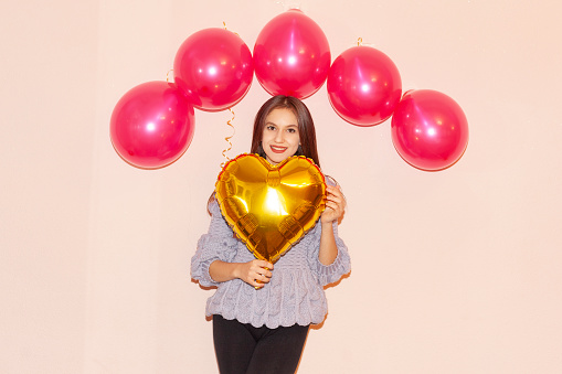 young beautiful girl in red dress embracing heart shaped golden air balloon. valentines day, birthday, womens day, anniversary, holiday celebration concept