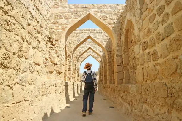 Photo of Man Walking Along the Iconic Archways in Bahrain Fort, Manama, Bahrain