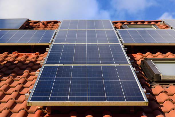 fundo e close-up de um painel solar em um telhado de um domicílio familiar com telhas vermelhas, de encontro a um céu azul com nuvens e luz do sol para a energia da luz solar - solar panel innovation renewable energy alternative energy - fotografias e filmes do acervo