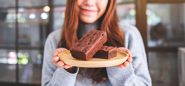 Closeup image of a beautiful asian woman holding a brownie cake in wooden plate