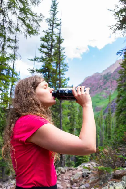 Young girl thirsty woman stopping for drinking water on hike on Snowmass Lake Trail in Aspen, Colorado in 2019 summer