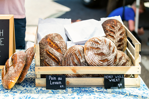 Closeup of fresh traditional baked sourdough bread loaves in bakery with signs for pain au levain and honey whole wheat with prices in farmers market