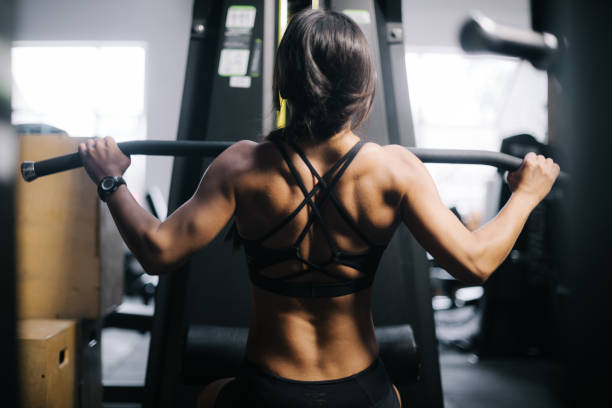 istock Muscular strong woman using training simulator for pumping back muscles 1197800755