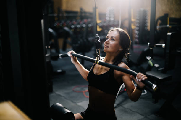 istock Athletic young woman using training simulator for pumping back muscles in gym 1197800817
