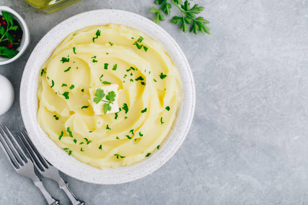 puré de papas con mantequilla y perejil fresco en un tazón blanco sobre fondo de hormigón de piedra gris. - mashed potatos fotografías e imágenes de stock