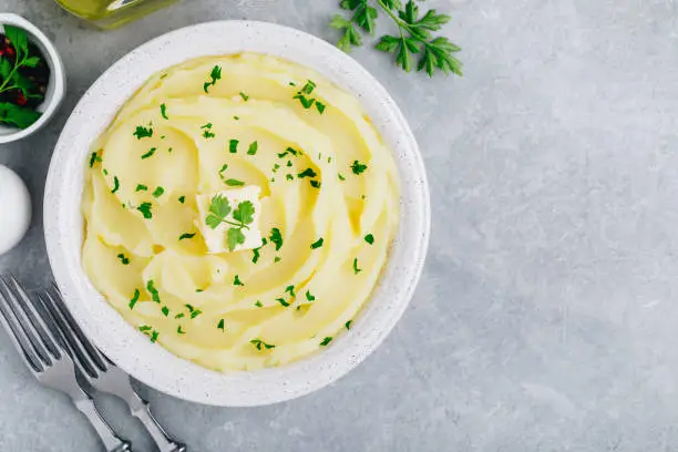 Mashed Potatoes with butter and fresh parsley in a white bowl on gray stone concrete background. Top view, copy space