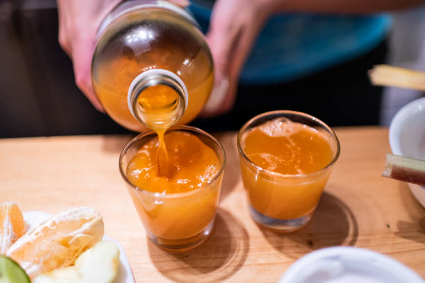 コンブチャ発酵茶をボトルから木製のテーブルの上の2つのジュースショットグラスに注ぐ女性 - apple juice ストックフォトと画像