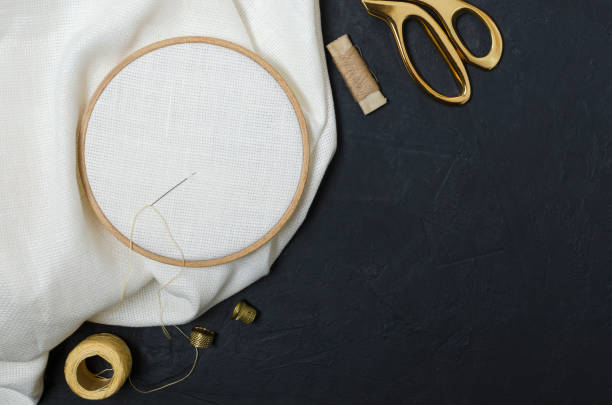 istock Top view of tools for embroidering. Golden scissors, threads, thimble, embroidery hoops, clean fabric on the black table 1197810897