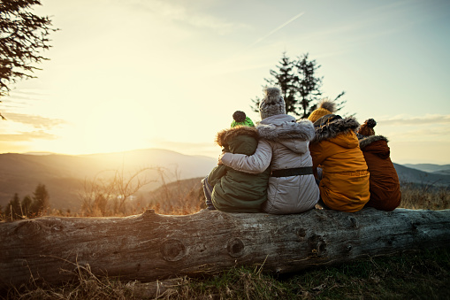 Mother and three kids hiking in mountains. Family is sitting on tree trunk and looking at sunset and view.\nCold winter or autumn day.\nNikon D850