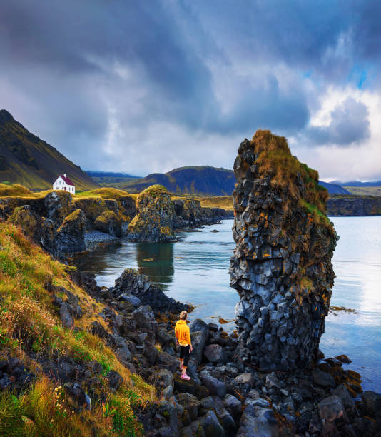 turista en una playa rocosa mira una pequeña casa en arnarstapi, islandia - snaefellsnes fotografías e imágenes de stock