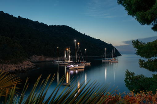 Moored sailboats in amazing bay near little town Assos at night. Situated on small peninsula on island of Kefalonia is famous tourist destination in Greece. Beautiful multicolored houses, traditional architecture and culture, clear blue sea attracts tourists from all over the world, but especially yacht and sailboat travelers because of calm sea in the bay and good shelter from prevailing winds.