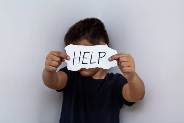 HELP, Teenager with help sign. Boy holding a paper with the inscription. Kid holding sheet of paper with word HELP on grey wall background. HELP, Teenager with help sign. Boy holding a paper with the inscription. Kid holding sheet of paper with word HELP on grey wall background. child abuse stock pictures, royalty-free photos & images