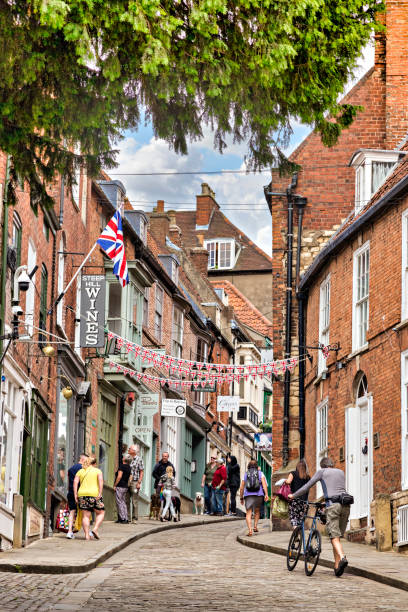 2 July 2019: Lincoln, UK - People walking and sightseeing in Steep Hill, the city's famous medieval street. One man pushing a bike up the hill.