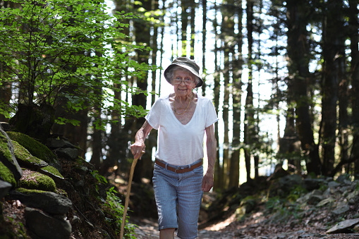 An old woman walks on a path with a cane in the forest