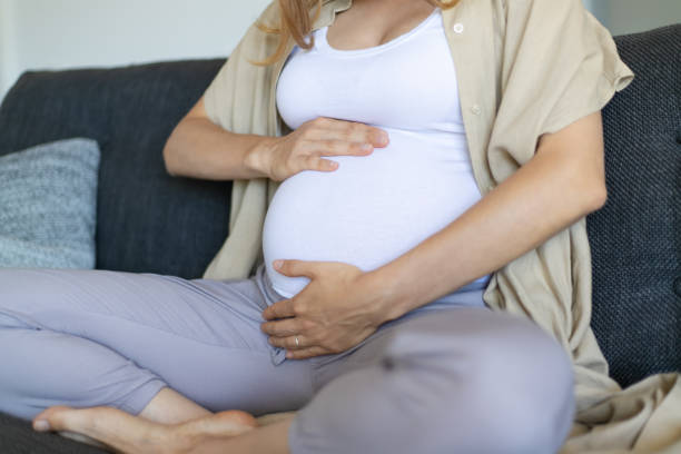 istock Expectant mother sitting on couch and embracing baby bump 1197828663