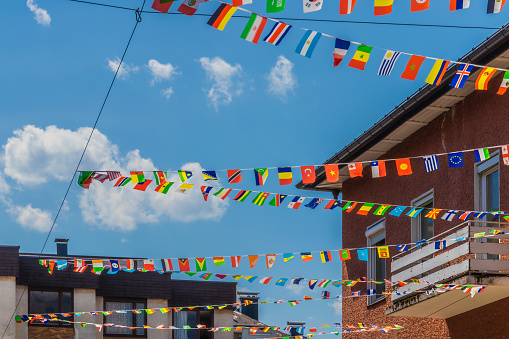 Colorful paper flags of different countries hanging on wires, blue sky and residential buildings in the background. International travel concept.