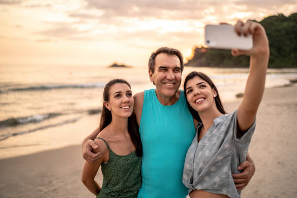 istock Father and daughters at the beach taking picture 1197834446