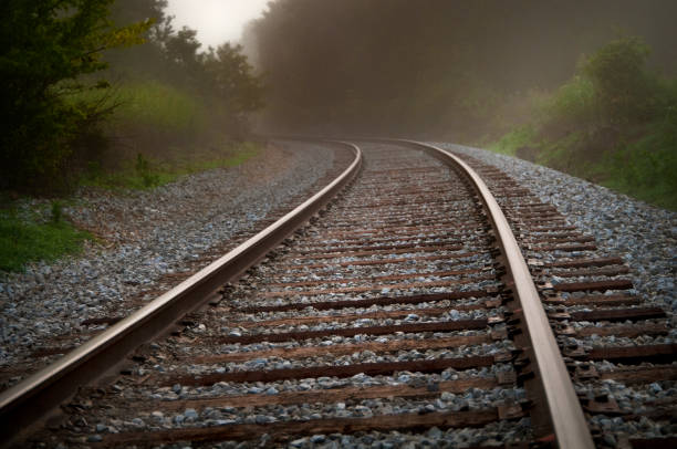 metal train tracks curve and off into the fog - railroad spikes imagens e fotografias de stock