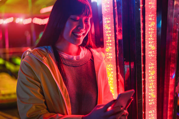 Happy asian girl using smartphone at amusement park - Young trendy woman having fun with tecnology trends with neons in backgrounds - Tech and youth concept - Soft focus on face chica asiática feliz usando el teléfono inteligente en el parque de atracciones - joven mujer de moda divirtiéndose con las tendencias de la tecnología con neones en los fondos - tecnología y concepto de la juventud - enfoque suave en la cara