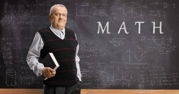 istock Mature math teacher with a book in front of a blackboard with formulas 1197840212