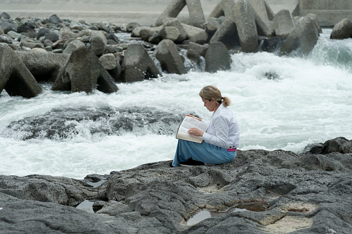 Young mixed race woman (Brazilian / Japanese) reading the bible by the Fujikawa river in Fuji City, Japan. Copy space. Horizontal shot.