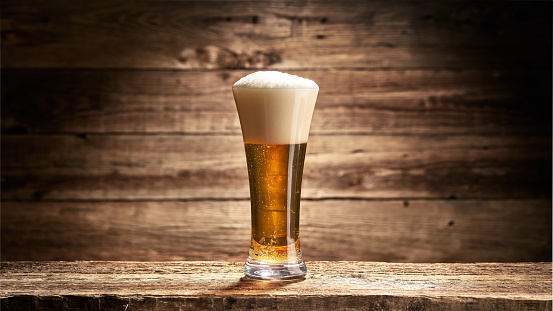 A glass full of beer with foam against the background of old boards