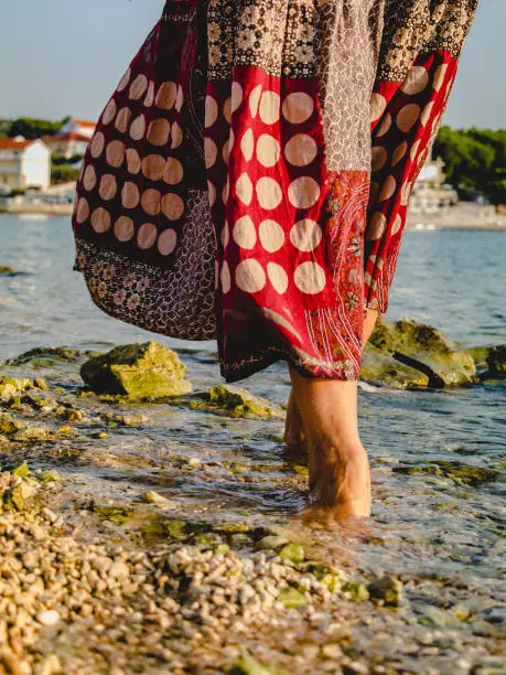 Photo of Summer vacation at sea. A barefoot woman walks on the stones by the sea early in the morning. The concept of a healthy lifestyle and freedom.