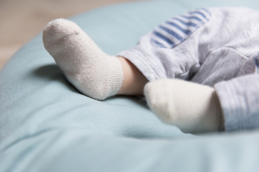Tiny feet of baby lying on soft blue mattress, wearing socks. Closeup of little child in home interior. Baby clothes concept
