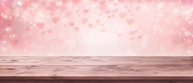 Flying pink hearts for valentines day. Abstract background and empty wooden table for a romantic love concept with space for design and text.