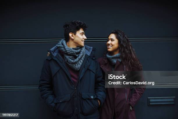 Portrait Of A Happy Young Hispanic Couple Smiling While Standing Together And Looking At Eachother Outside Stock Photo - Download Image Now