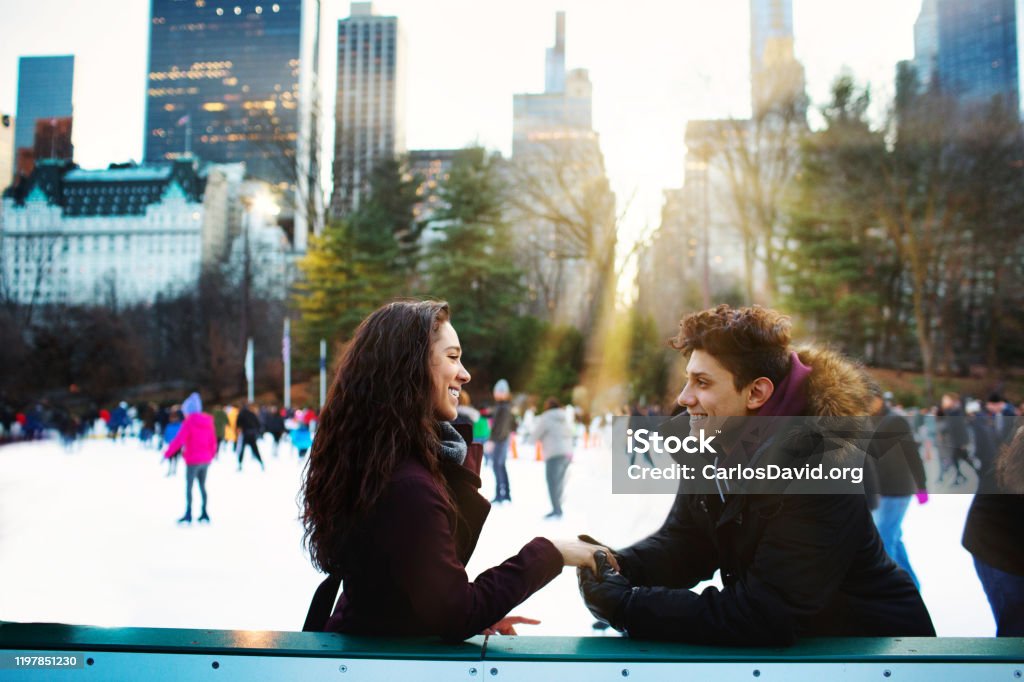 Portrait of a happy young  couple smiling and holding each other while ice skating outside in Central Park on a sunny day Ice-skating Stock Photo