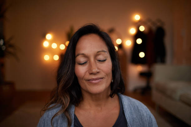 Mature woman smiling while meditating with her eyes closed at home
