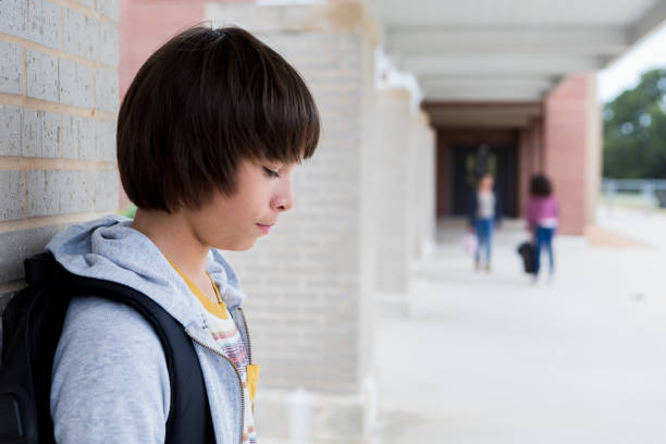 Depressed schoolboy standing on school campus Downcast schoolboy looks down while standing on a middle school campus. school exclusion stock pictures, royalty-free photos & images