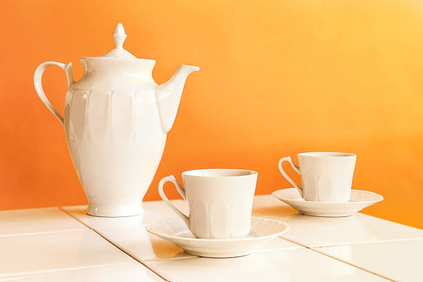 Set of white tea cups and teapot on white tiles table.