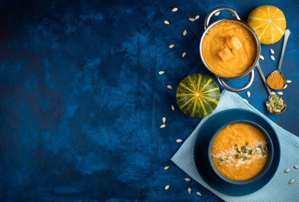 pumpkin cream soup in a blue plate on a deep classic blue background with slices of pumpkin with blue textile and a spoon. flat lay pumpkin cream soup in a blue plate on a deep classic blue background with slices of pumpkin with blue textile and a spoon. flat lay. food styling stock pictures, royalty-free photos & images