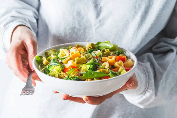 Photo of Valentine's Day concept. Woman eats salad with pasta hearts, olives, tomatoes, spinach and broccoli.