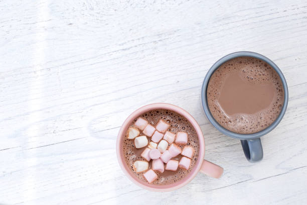istock Hot chocolate in two mugs, one with small marshmallows, isolated on white painted wood from above. Space for text. 1197866613