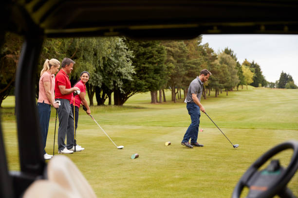 istock Two Couples Golfing Hitting Tee Shot Along Fairway With Driver With Buggy In Foreground 1197866731