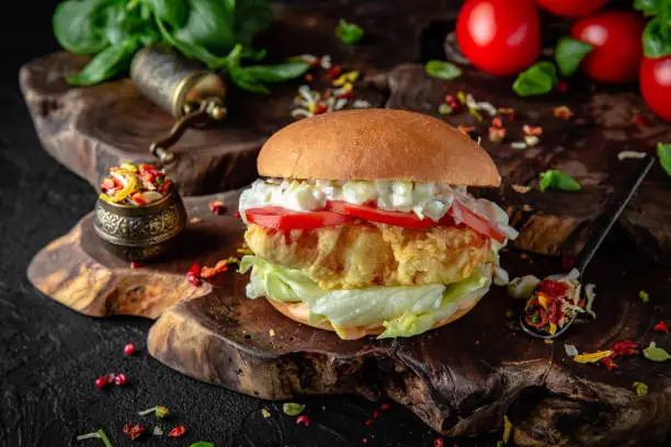 Tasty grilled burger with chicken or fish (salmon) breaded, vegetables, lettuce, sauce  Delicious grilled Fishburger or chickenburger on a dark background. Free space for text