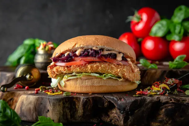 Tasty grilled burger with chicken or fish (salmon) breaded, vegetables, lettuce, sauce  Delicious grilled Fishburger or chickenburger on a dark background. Free space for text