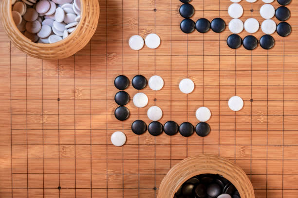istock Go board game playing. A competitor is placing a marble piece on a Go board game, Hand playing black and white stone pieces on 1197883450
