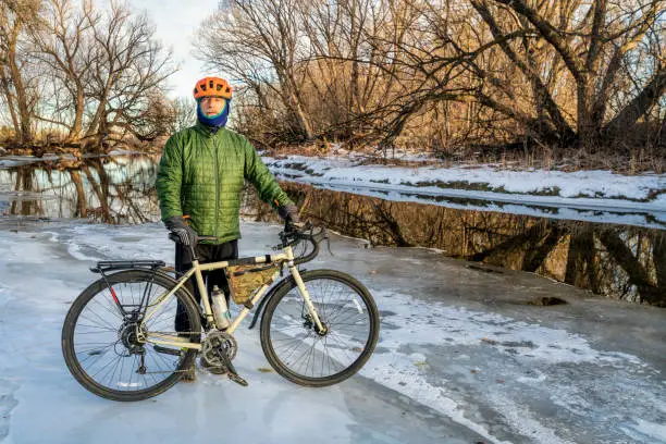 senior male cyclist with a touring bike on an icy river shore, Poudre River in Fort Collins, Colorado, winter biking or commuting concept