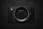 Empty black dish and cutlery on black table. Black table arrangement