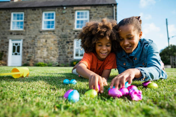 Easter with My Brother! A front-view shot of a young boy with an afro and his older sister, they are lying down on their front smiling while holding their Easter eggs. egg food photos stock pictures, royalty-free photos & images